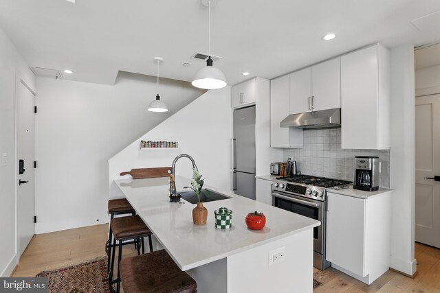 kitchen featuring appliances with stainless steel finishes, under cabinet range hood, a sink, a breakfast bar area, and white cabinetry