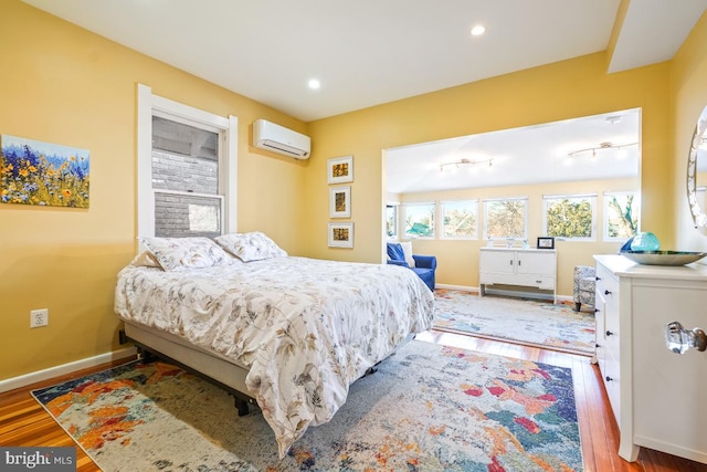 bedroom featuring recessed lighting, baseboards, a wall mounted AC, and wood finished floors
