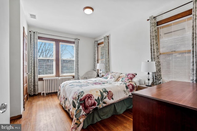 bedroom with visible vents, radiator heating unit, and hardwood / wood-style floors