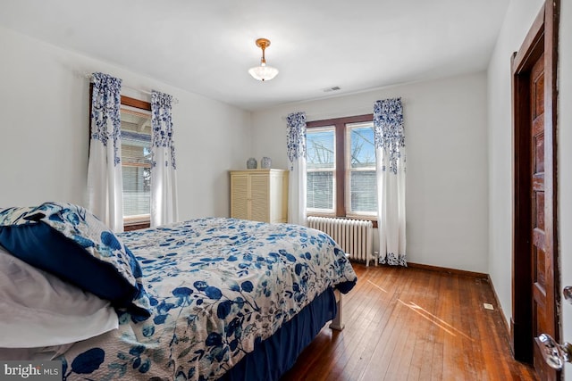 bedroom featuring wood-type flooring, baseboards, visible vents, and radiator heating unit