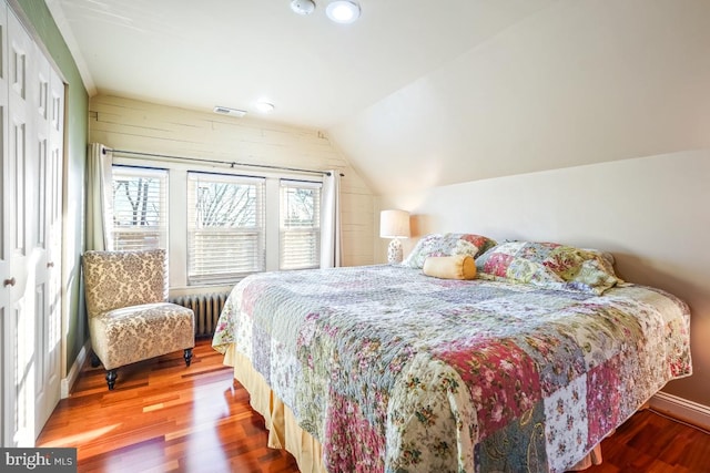 bedroom featuring radiator heating unit, baseboards, wood finished floors, lofted ceiling, and visible vents