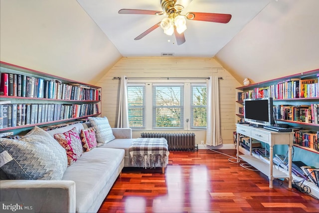 sitting room featuring a ceiling fan, vaulted ceiling, wood finished floors, wooden walls, and radiator heating unit