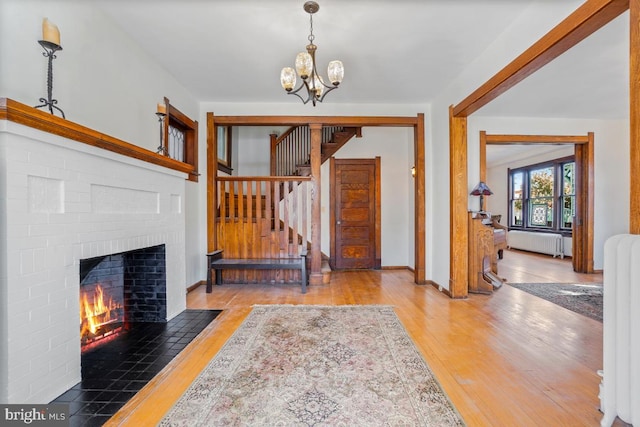 foyer entrance featuring an inviting chandelier, radiator, a brick fireplace, stairs, and hardwood / wood-style flooring