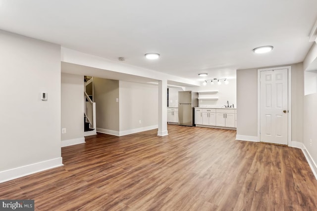 unfurnished living room with a sink, baseboards, stairs, and wood finished floors