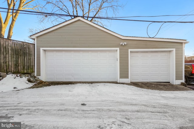 snow covered garage featuring a garage and fence