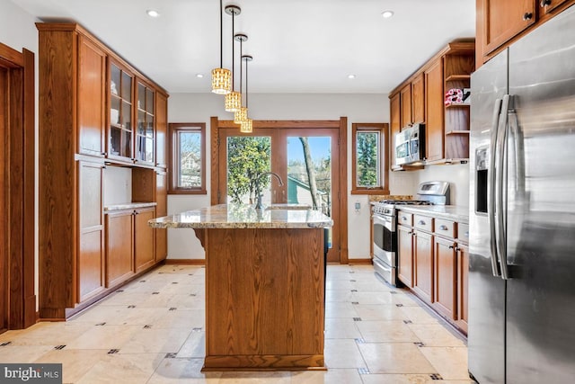 kitchen featuring open shelves, light stone countertops, an island with sink, brown cabinets, and stainless steel appliances