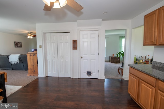 kitchen with dark wood-style flooring, ceiling fan, brown cabinetry, and dark stone countertops