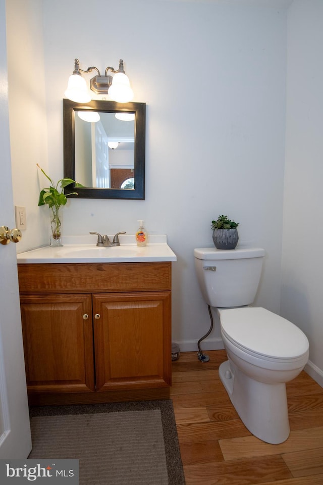 half bathroom with vanity, baseboards, wood finished floors, and toilet