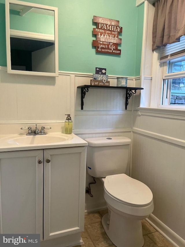 half bathroom with a wainscoted wall, toilet, vanity, and tile patterned floors