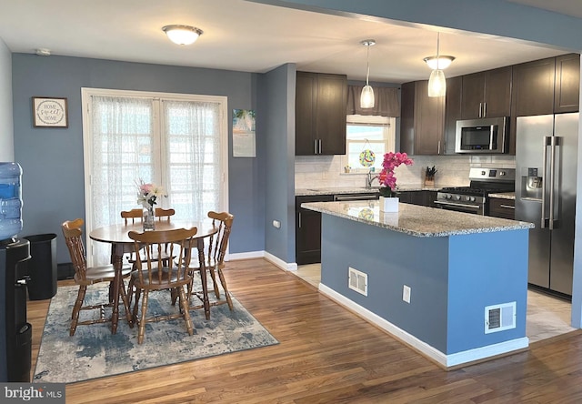 kitchen with appliances with stainless steel finishes, backsplash, light wood-type flooring, and baseboards