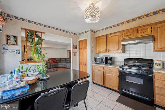 kitchen featuring gas stove, light countertops, light tile patterned floors, stainless steel microwave, and under cabinet range hood