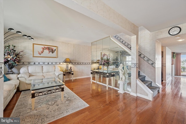 living room featuring baseboards, wallpapered walls, wood finished floors, and stairway