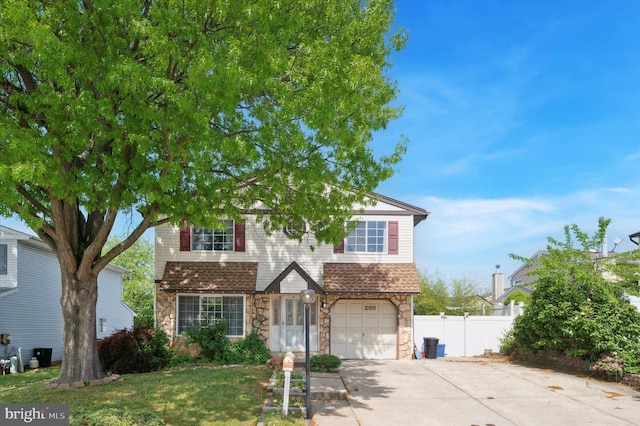 traditional-style home featuring a garage, fence, stone siding, and concrete driveway