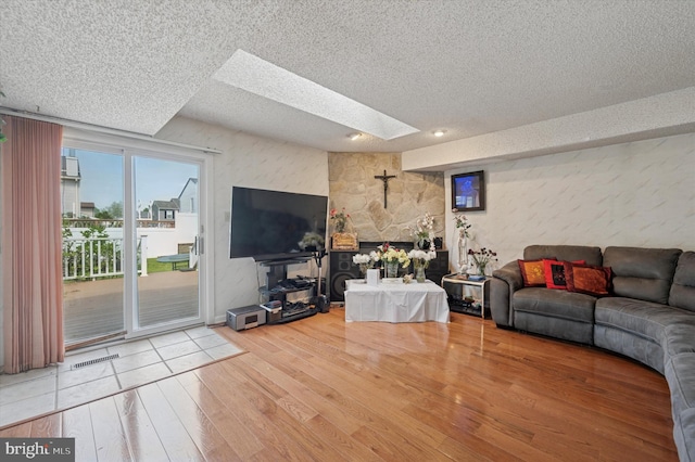 living room with visible vents, a textured ceiling, wood finished floors, and a skylight