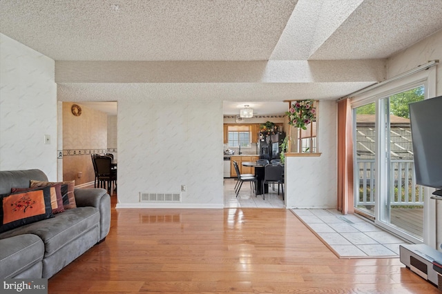 living area featuring visible vents, light wood-style flooring, and a textured ceiling