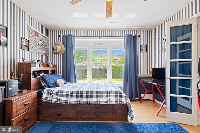 bedroom with wood finished floors, visible vents, a baseboard radiator, ceiling fan, and wallpapered walls