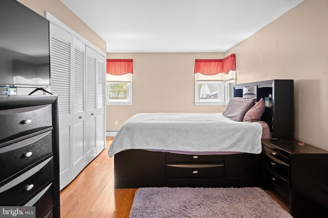 bedroom featuring a closet, light wood-type flooring, and a baseboard heating unit