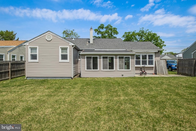 rear view of property featuring a lawn, a shingled roof, and fence