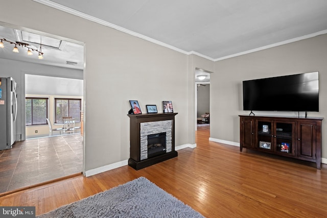 living room featuring a stone fireplace, wood finished floors, baseboards, and ornamental molding