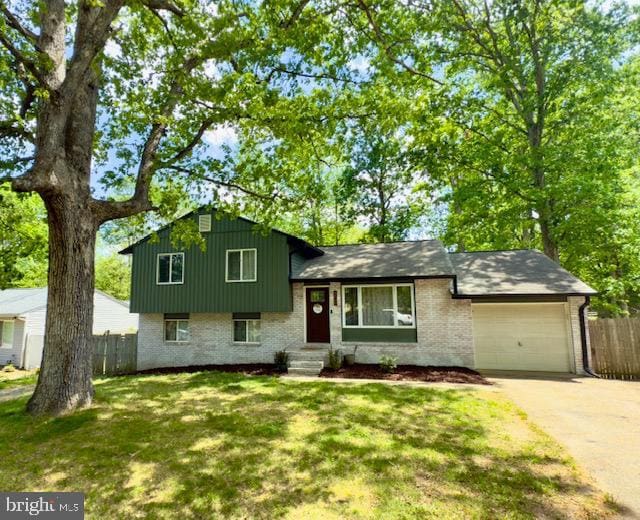 tri-level home featuring board and batten siding, driveway, a garage, brick siding, and fence