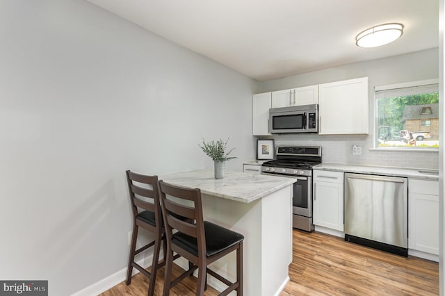 kitchen with decorative backsplash, appliances with stainless steel finishes, a breakfast bar area, and white cabinets