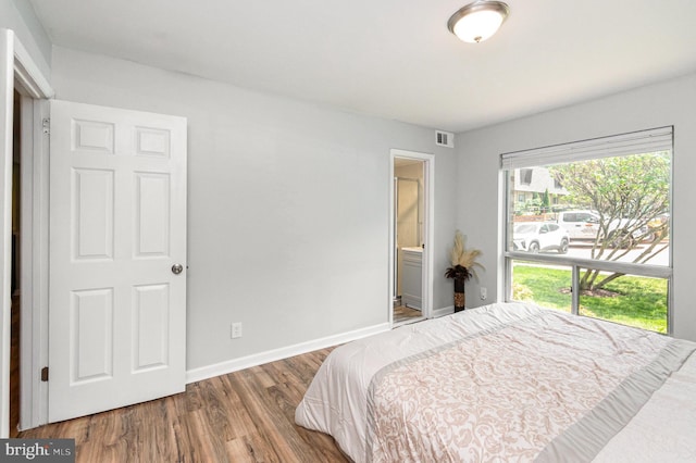 bedroom with baseboards, visible vents, wood finished floors, and ensuite bathroom