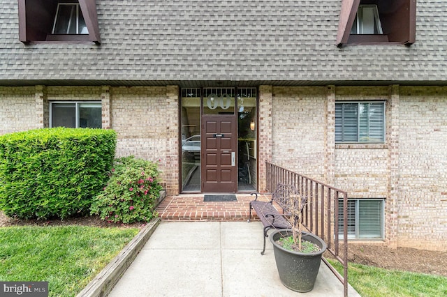 property entrance featuring brick siding and a shingled roof