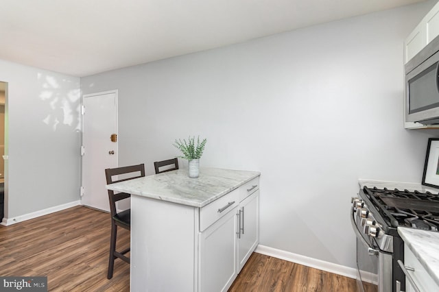 kitchen featuring a kitchen breakfast bar, dark wood-style flooring, appliances with stainless steel finishes, baseboards, and white cabinets