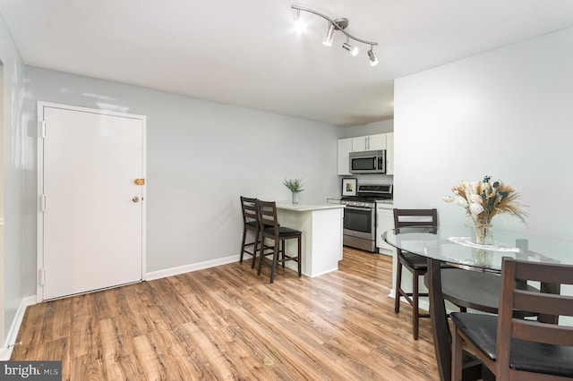 kitchen featuring a kitchen bar, light countertops, white cabinetry, light wood-style flooring, and stainless steel appliances