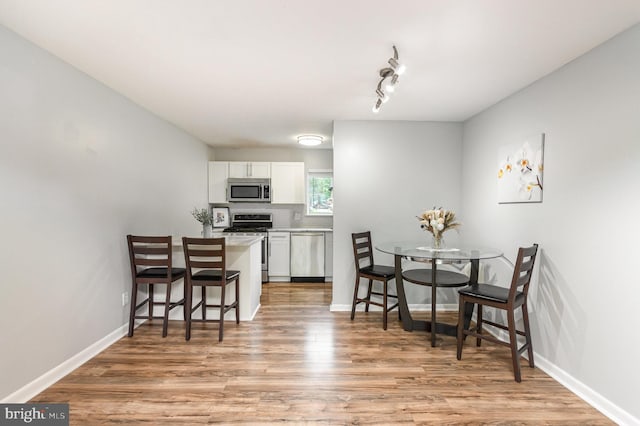 kitchen with white cabinets, light wood finished floors, light countertops, stainless steel appliances, and a kitchen bar