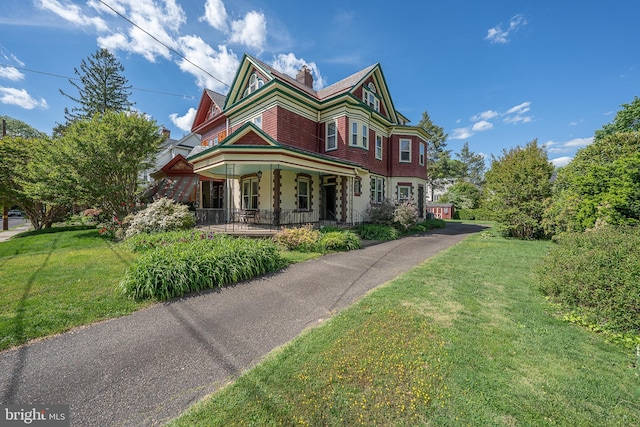 victorian-style house with a porch, a front yard, and a chimney
