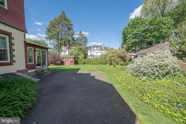 view of grassy yard with entry steps, a storage shed, an outbuilding, a residential view, and a patio area