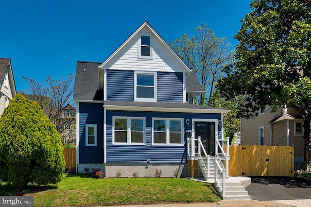 view of front facade with fence, a shingled roof, and a front lawn