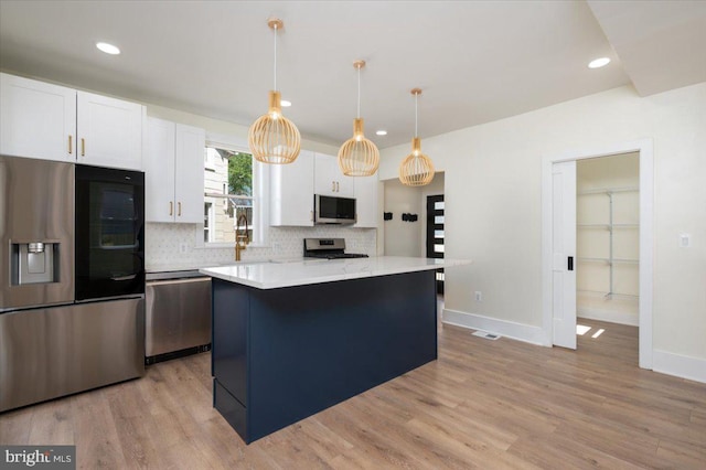 kitchen with white cabinets, appliances with stainless steel finishes, light countertops, a center island, and tasteful backsplash