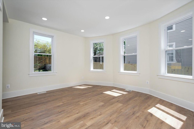 spare room with baseboards, visible vents, a healthy amount of sunlight, and wood finished floors