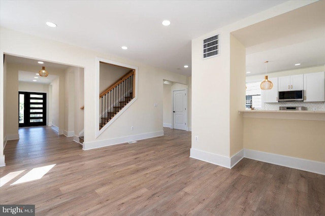 unfurnished living room featuring a healthy amount of sunlight, recessed lighting, light wood-style floors, and stairs