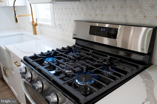 room details with stainless steel range with gas cooktop, a sink, light stone counters, and white cabinets