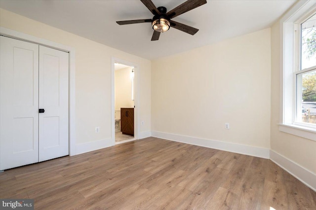 unfurnished bedroom with a closet, wood finished floors, baseboards, connected bathroom, and a ceiling fan
