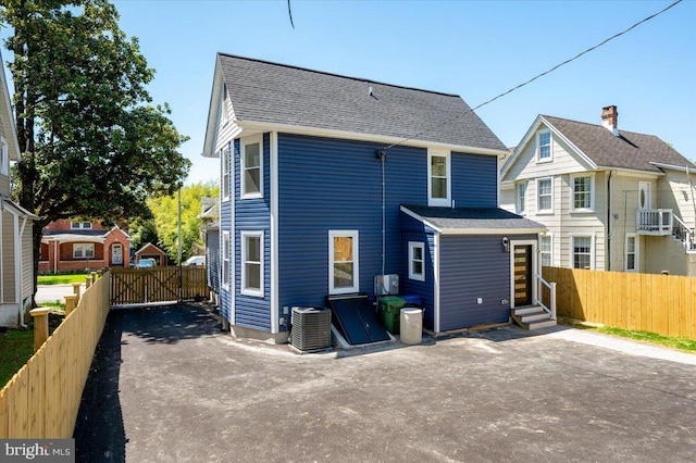 rear view of house with entry steps, fence, central air condition unit, and roof with shingles