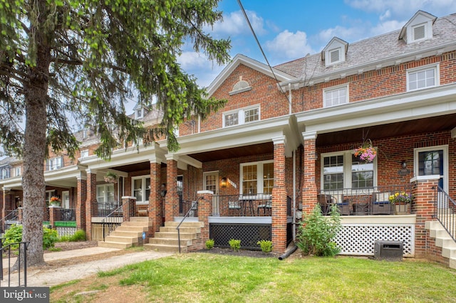 view of property featuring covered porch, brick siding, and a front yard