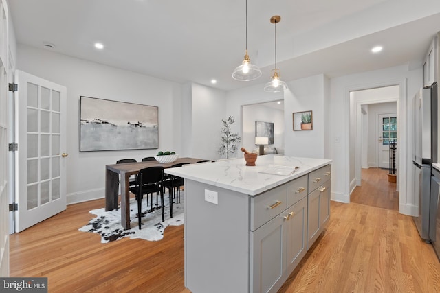 kitchen with light stone counters, light wood finished floors, a center island, gray cabinetry, and pendant lighting