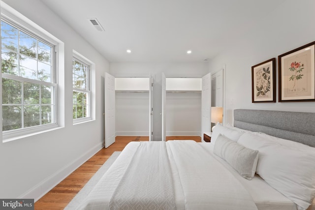 bedroom featuring light wood finished floors, multiple closets, recessed lighting, baseboards, and visible vents