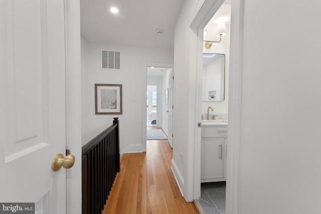 corridor featuring a sink, baseboards, light wood-type flooring, and visible vents
