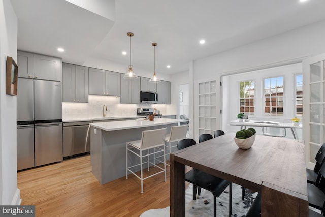 kitchen featuring appliances with stainless steel finishes, a sink, gray cabinetry, light countertops, and light wood finished floors