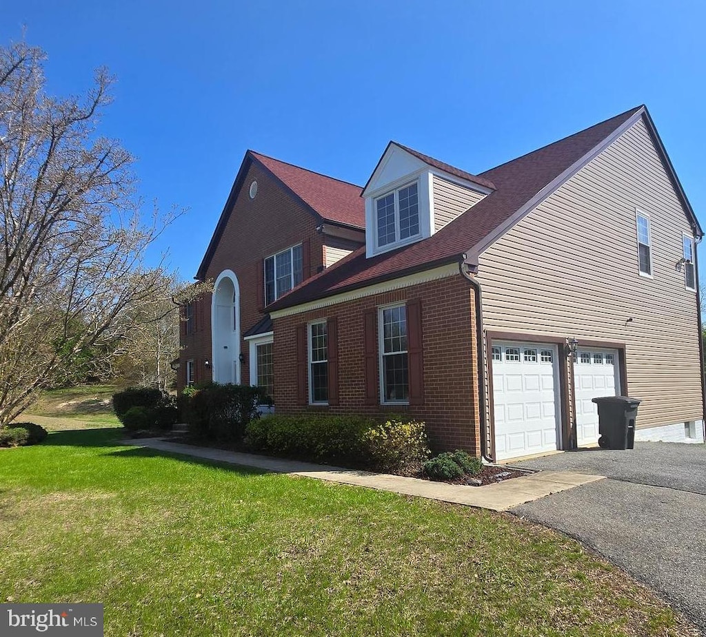 view of side of property with an attached garage, a yard, driveway, and brick siding