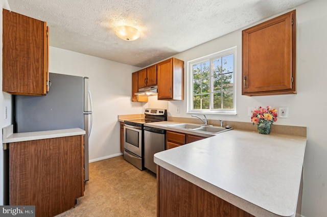 kitchen with a sink, appliances with stainless steel finishes, a textured ceiling, brown cabinets, and baseboards