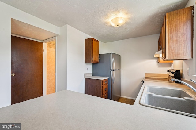 kitchen with appliances with stainless steel finishes, under cabinet range hood, a sink, brown cabinetry, and light countertops