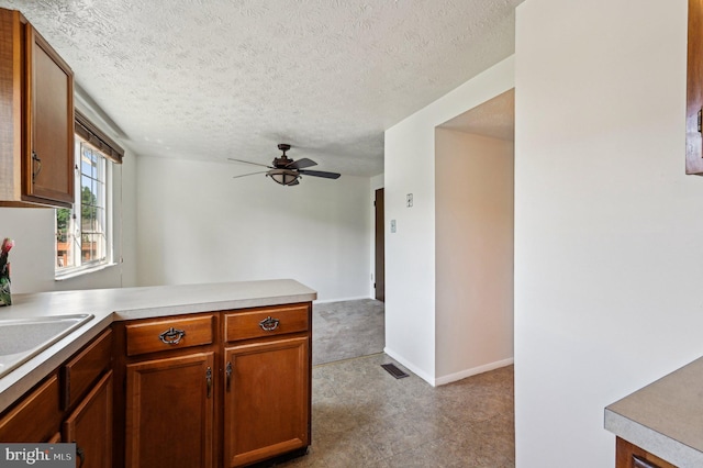 kitchen featuring a textured ceiling, a peninsula, light countertops, ceiling fan, and brown cabinets