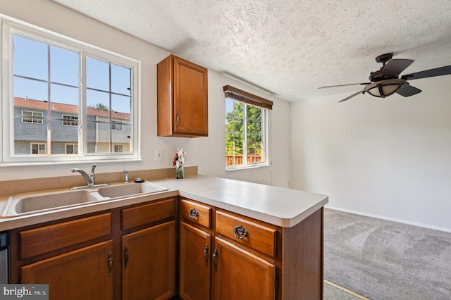 kitchen with a sink, a peninsula, a textured ceiling, light countertops, and a ceiling fan
