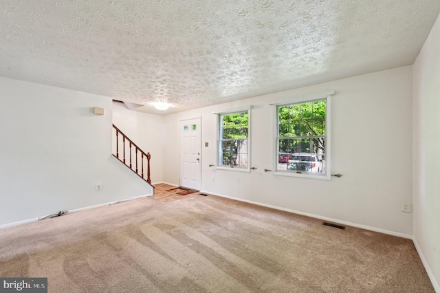 unfurnished living room with stairway, carpet floors, a textured ceiling, and baseboards